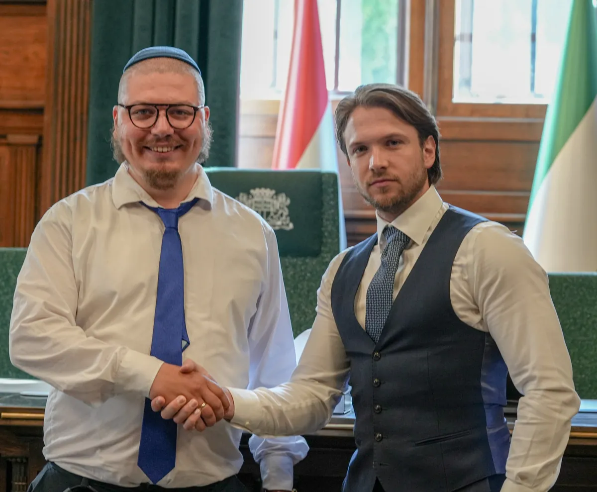 Uścisk dłoni w sali obrad, w tle flagi i zielone fotele